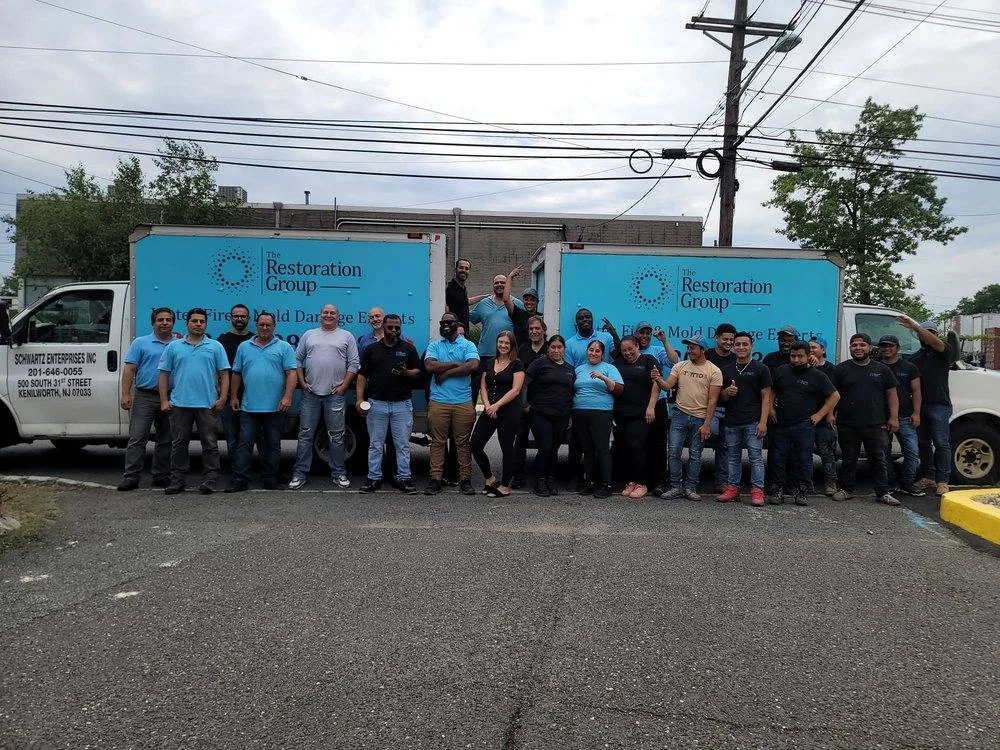 The The Restoration Group team lined up in front of two lettered company box trucks outside the company headquarters in northern New Jersey